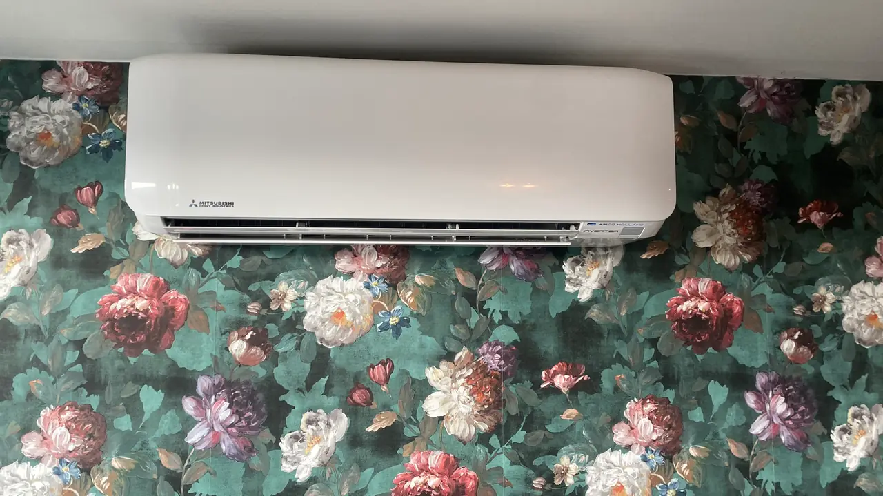 Een wit binnendeel van Mitsubishi Heavy Industries aan een muur met donkergroen rozenbehang, zonder zichtbare leiding.