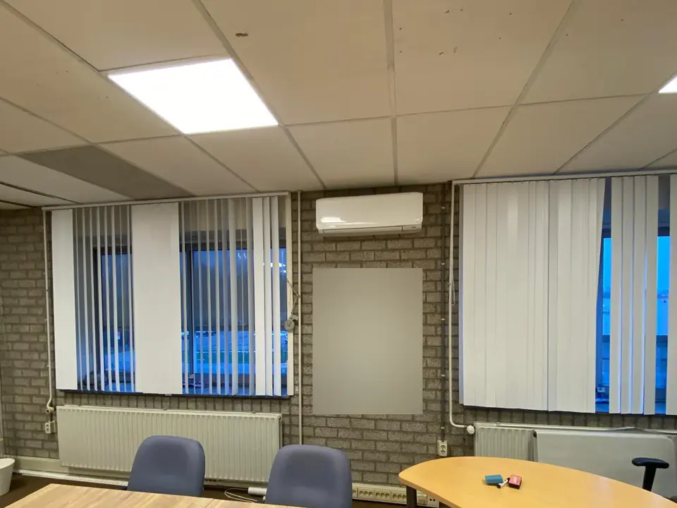 Een wit binnendeel tussen twee ramen in een vergaderruimte met een bakstenen muur, een whiteboard en tafels.