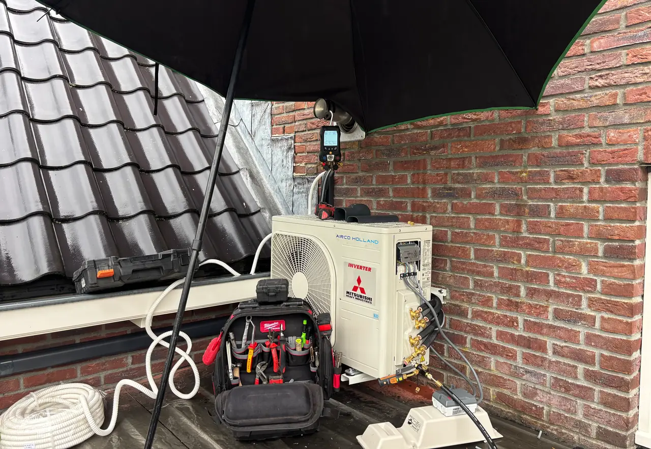 Een buitendeel van Mitsubishi Heavy Industries met twee sets leidingen wordt aangesloten onder een zwarte paraplu.