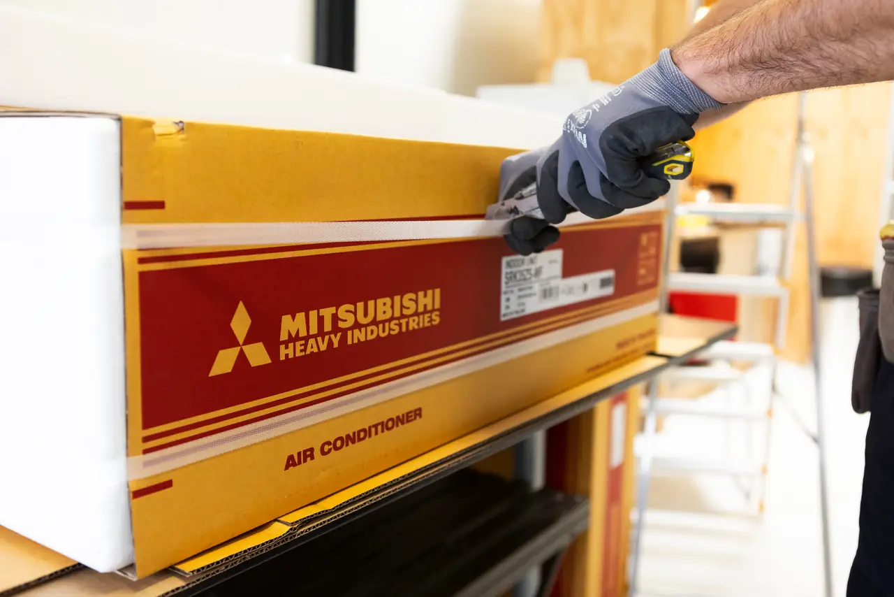 Een gehandschoende hand snijdt de tape van een doos van Mitsubishi Heavy Industries open.