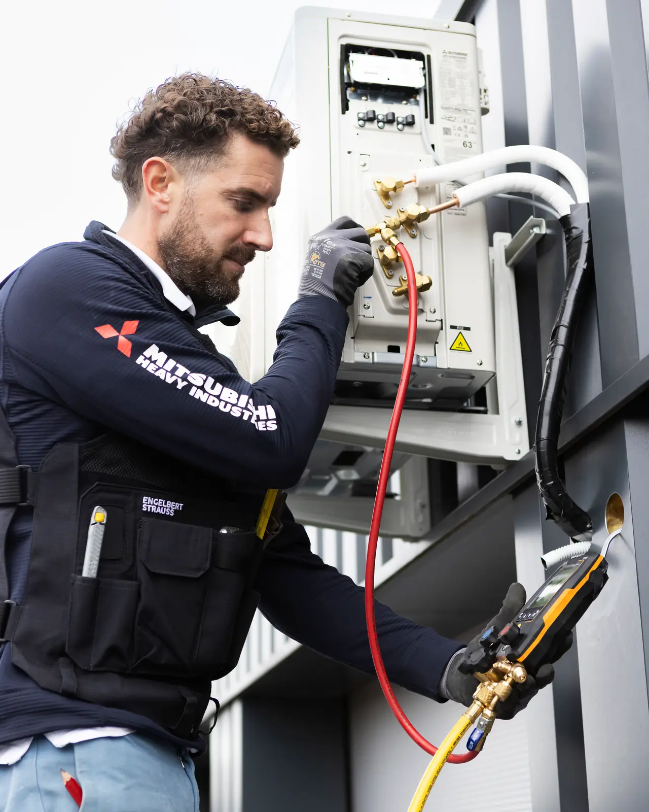 Rein trekt een nieuwe buitenunit vacuüm, met een digitale meter en een rode en een gele slang aan de kranen.