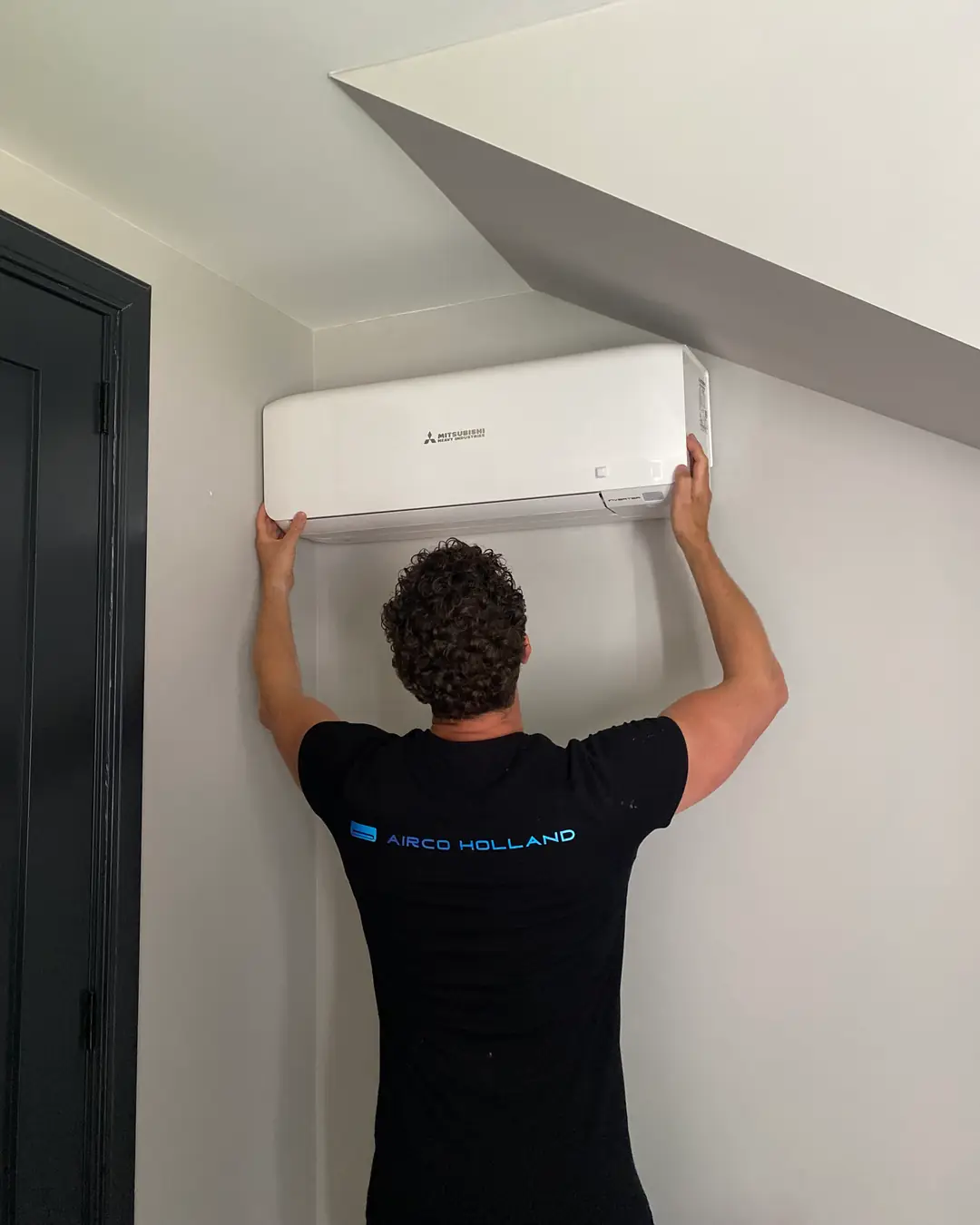 Rein, van achteren, houdt een wit wandmodel van Mitsubishi Heavy Industries tegen de muur onder een schuin plafond.