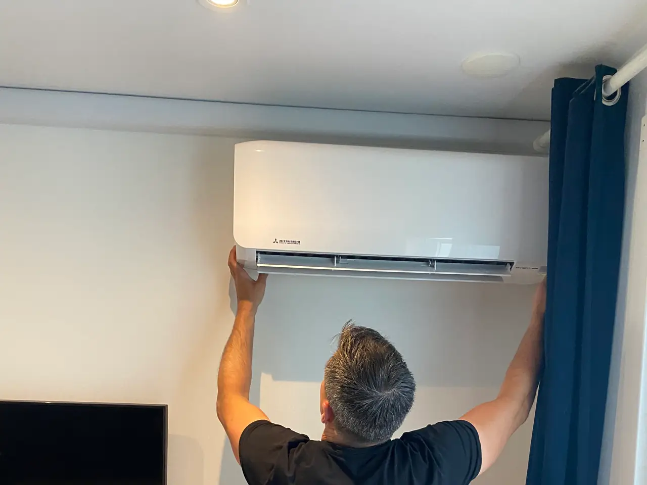 Peter hangt een wit wandmodel van Mitsubishi Heavy Industries op, onder een witte goot langs het plafond.