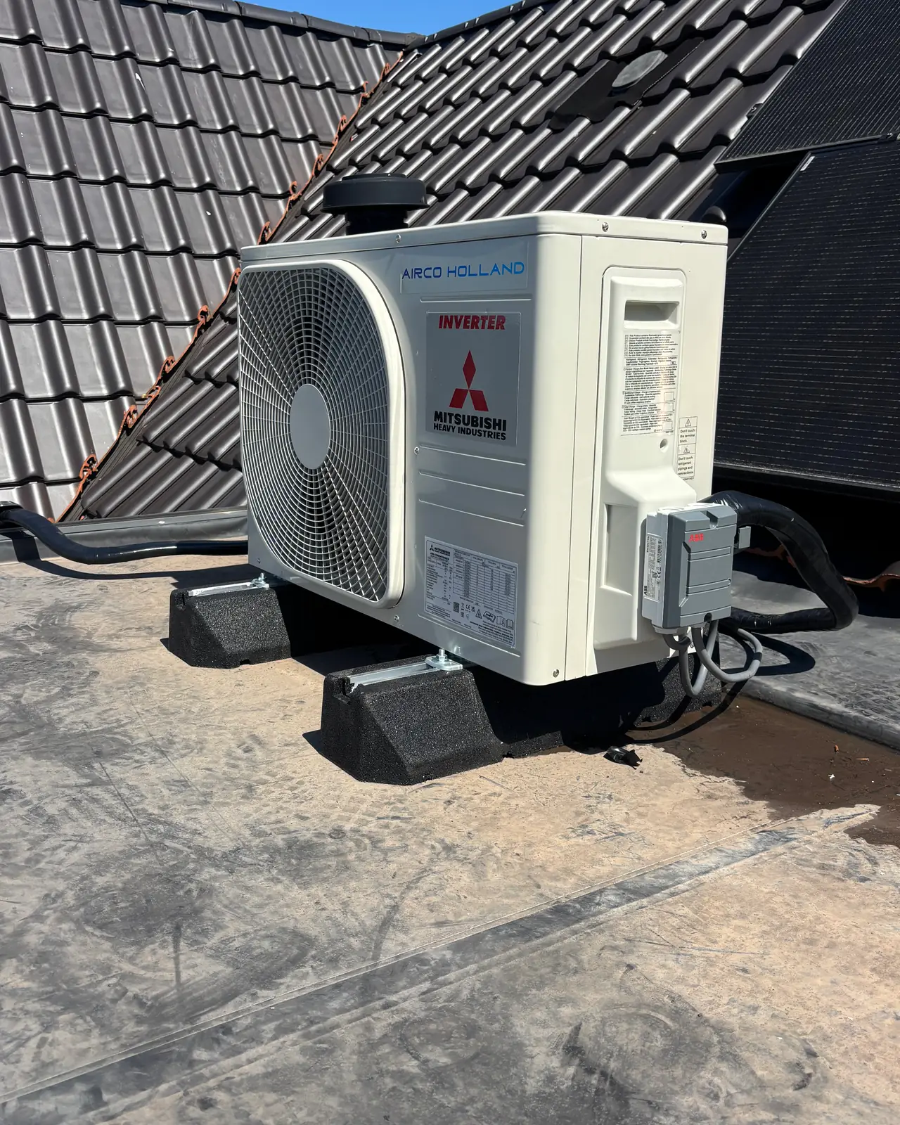 Een nieuw buitendeel van Mitsubishi Heavy Industries met Airco Holland erop, op rubberen voeten op een plat dak.
