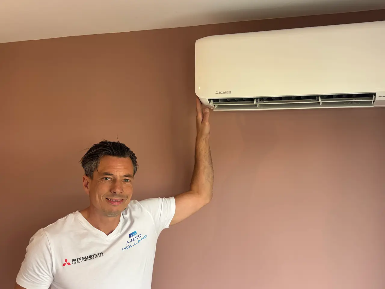 Peter in een wit shirt houdt zijn hand onder een nieuw wit binnendeel aan een oudroze muur.