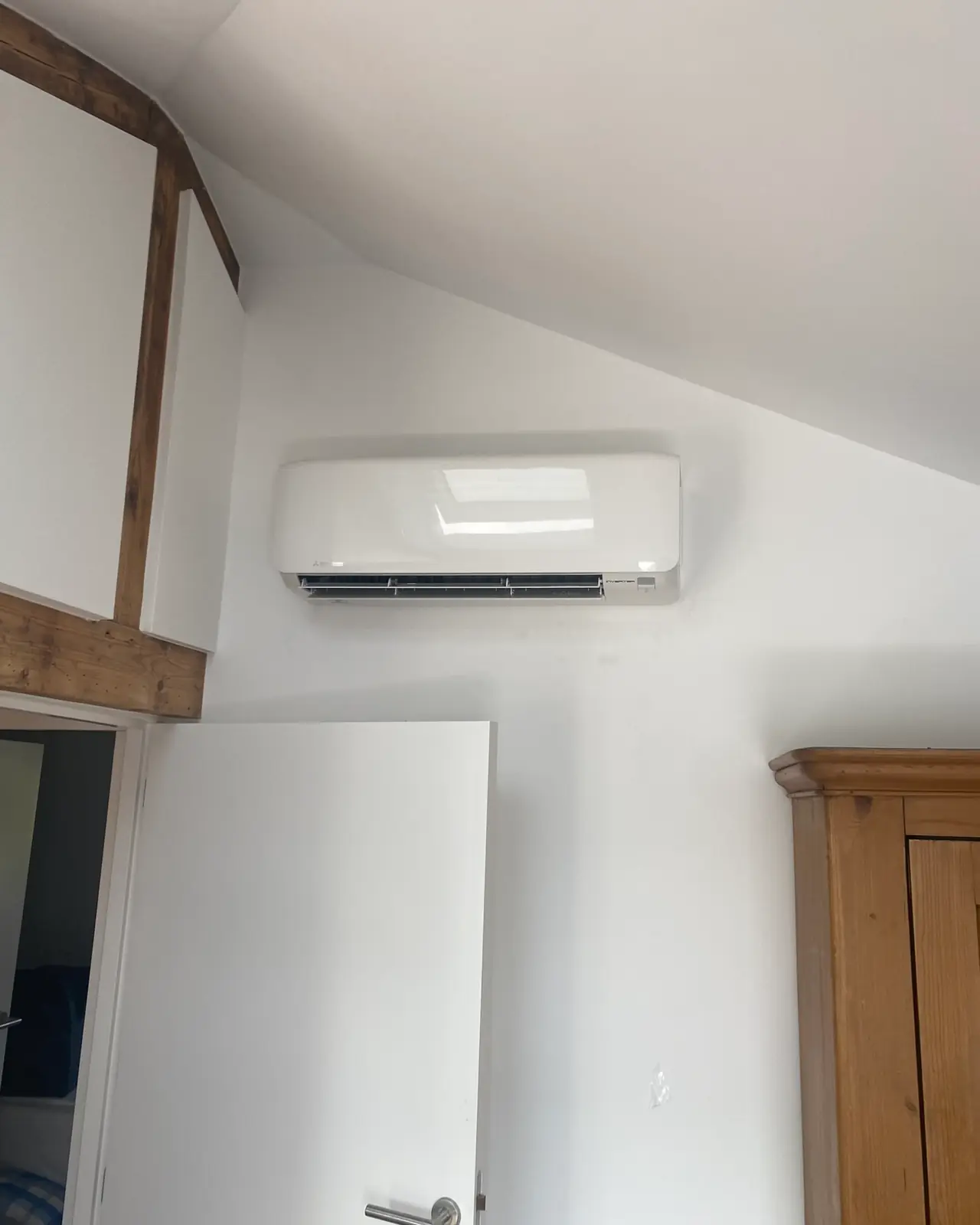 Een wit wandmodel boven de deur van een zolderkamer met een houten balk, zonder zichtbare leiding.
